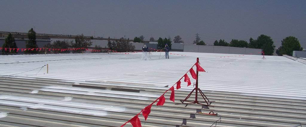 two commercial roof employees applying a white roof coating to a metal roof