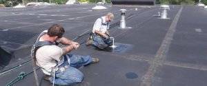 commercial roof technicians install a horizontal lifeline on a flat commercial roof as a fall protection option
