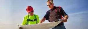 two men looking at building plans on roof